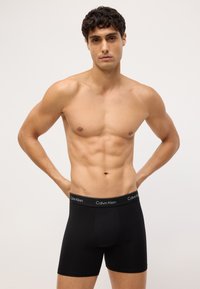 Czarne bawełniane bokserki z dopasowanym krojem i elastycznym paskiem wbudowanym z logo "Calvin Klein". Gładka tekstura i cylindryczny kształt.