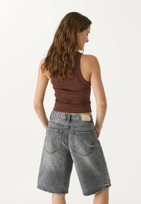 Un débardeur marron côtelé associé à un short en denim gris taille haute avec un ourlet brut, cinq poches et une patte en cuir avec logo.
