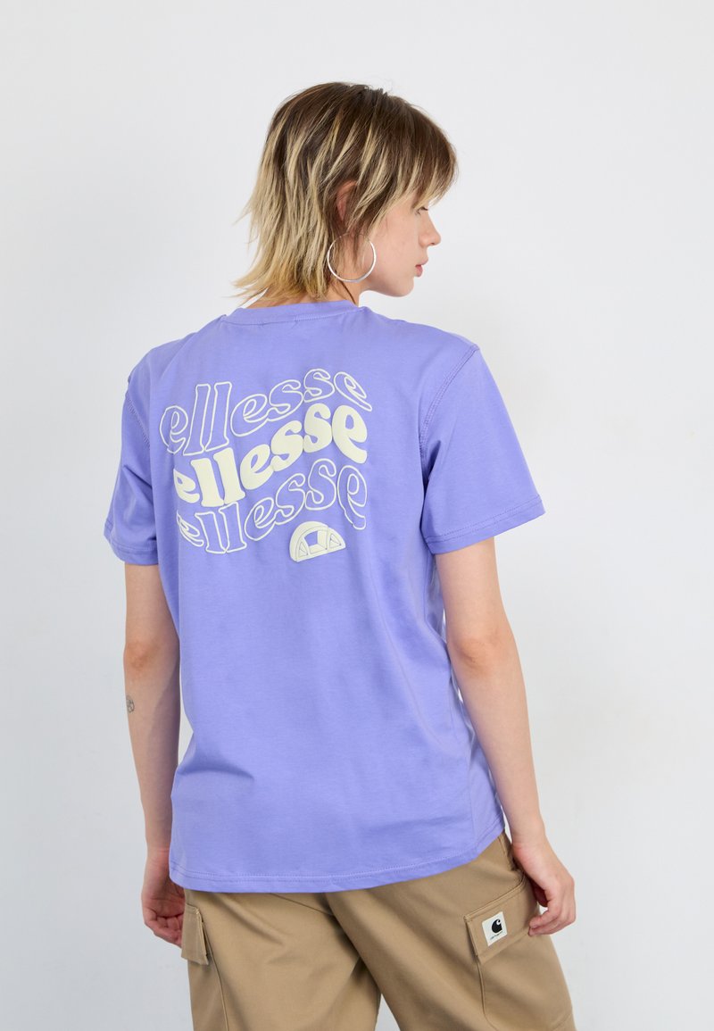 Light purple cotton t-shirt featuring white text print on the back. Crew neck, short sleeves, and relaxed fit. Worn with khaki cargo pants.