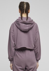 Hoodie accorciato in lavanda tenue, realizzato in tessuto morbido. Presenta un grande cappuccio, vestibilità rilassata e orlo a costine. Visibili i polsini testurizzati.