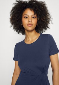 Granatowa sukienka z t-shirta wykonana z miękkiego materiału. Posiada krótkie rękawy, okrągły dekolt oraz skręcony detal w okolicy pasa.