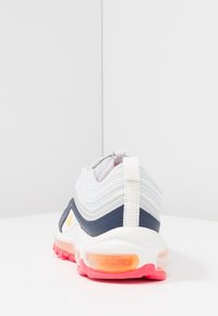 Weißer und marineblauer Sneaker mit wellenförmigem Textil-Obermaterial, weißer Sohle, durchsichtiger orangefarbener Air-Einheit und pinker Laufsohle; verfügt über eine Zuglasche an der Rückseite.