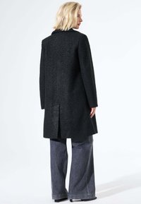 Zwarte textuurjas met een kraag, een rugventilatie en een rechte snit, gecombineerd met brede grijze denim broeken.