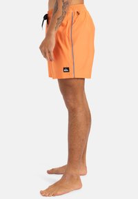 Bañador naranja hecho de tejido ligero, con una franja lateral azul y un parche de logo negro. Cintura elástica con cordón.