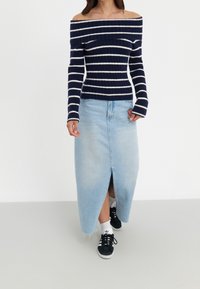Marineblauw en witte gestreepte off-shoulder trui met lange mouwen, gecombineerd met een lichtblauwe denim maxi rok met een split aan de voorkant. Zwarte sneakers.