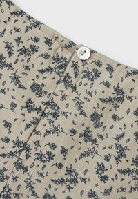 Ljus beige tyg med marinblå blommönster; har en knäppning bak och en texturerad yta.