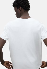 Camiseta de algodón blanca con cuello redondo y mangas cortas, vista desde la parte de atrás. Textura suave, ajuste casual y sin patrones visibles.