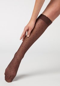 Braune Polka-Dot-Kniestrümpfe mit transparenter Oberfläche, ausgestattet mit einem glatten, gewellten Oberschenkelbund und einer engen Passform am Bein.