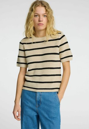 Beige stickad t-shirt med svarta ränder, korta ärmar och rund halsringning. Matchad med blå denimbyxor med en avslappnad passform.