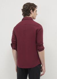 Chemise bordeaux à manches longues avec un col pointu, des poignets retroussés et un ourlet légèrement arrondi. Texture lisse et tissu léger.