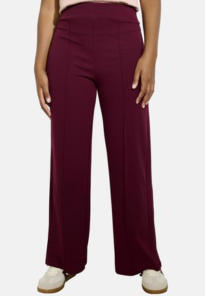 Burgundy wide-leg pants made of a stretchy material, featuring front seam details and a high waistband, paired with white sneakers.