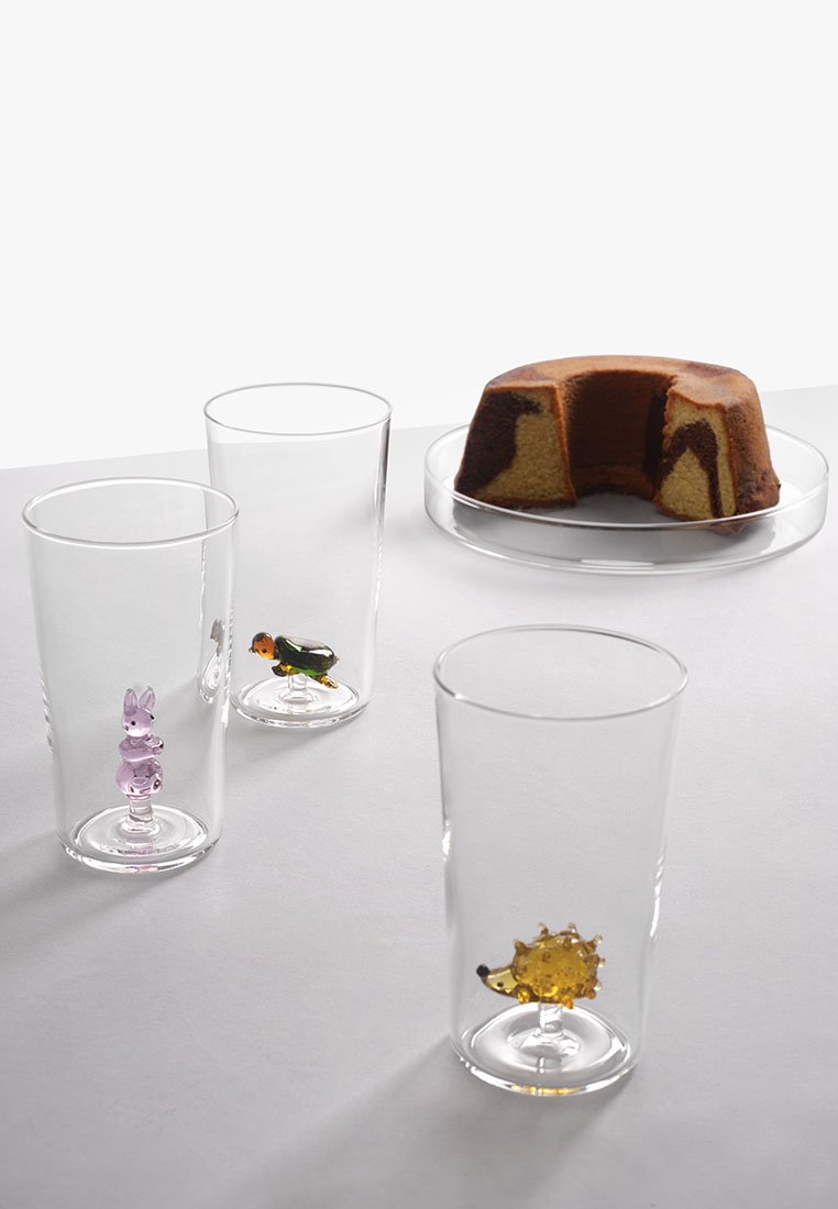 Przezroczyste szklanki mają kolorowe figury zwierząt w środku: fioletowego zająca, zieloną kaczkę i żółwia jeża; w towarzystwie okrągłego ciasta.