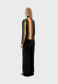 Maglietta a maniche lunghe, aderente, con strisce verticali multicolori in blu, arancione, marrone e crema; abbinata a pantaloni neri a gamba larga.