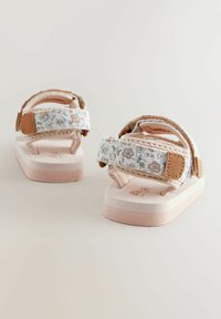 Helle rosa Sandalen mit floralen Stoffriemen und braunen Akzenten. Flache Sohle mit strukturierter Oberfläche und Klettverschlüssen für einen sicheren Halt.