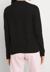 Suéter negro de tejido de punto con textura acanalada, cuello redondo, mangas largas y un corte holgado. Combinado con pantalones rosa claro.