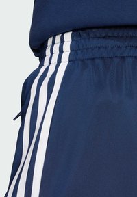 Mörkblå sportshorts med vita ränder längs sidorna, med ett elastiskt midjeband och en dragkedjeficka på sidan.