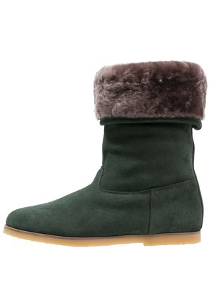 Botte de cheville en daim vert avec un revers en fausse fourrure marron, bout arrondi et semelle en caoutchouc plate. Texture lisse, design minimaliste et sans fermetures visibles.