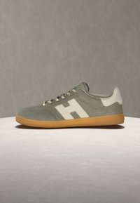 Γκρι σουέντ αθλητικό παπούτσι με λευκή φτέρνα και μεγάλο λευκό λογότυπο "H" στο πλάι, καφέ λαστιχένια σόλα και γκρι κορδόνια σε ουδέτερο φόντο.