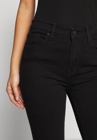 Zwarte spijkerbroek van denim met een getailleerd ontwerp, voorzien van voorzakken, een knoopsluiting en een gladde textuur. Minimale stikseldetails.