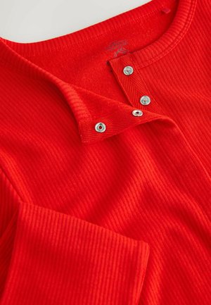 Punainen ribattuja pitkähihaista puseroa, jossa on pyöreä pääntie, nepparilista ja pehmeä pinta. Kankaassa on vaakasuoria viivoja.