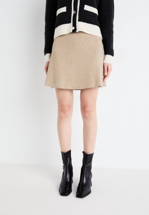Cardigan noir et crème avec des boutons, associé à une jupe beige qui s'évase doucement. Porté avec des bottines noires à talons, avec un bout carré.