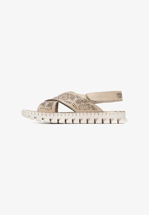 Sandalias beige perforadas con correas cruzadas, suela blanca texturizada y correa en el talón para soporte.