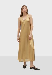 Zlaté maxi šaty bez rukávů s kulatým výstřihem, vyrobené z lesklé, hladké tkaniny. Černé špičaté baleríny s akcenty z kamínků.