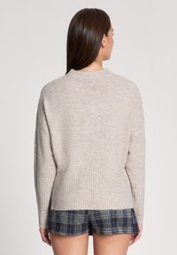 Beżowy, oversize sweter z okrągłym dekoltem i ściągaczem; miękka tekstura z delikatnym wzorem. Nosisz go na granatowych, wzorzystych szortach.