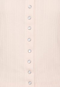 Różowa żebrowana bluzka dzianinowa z zapięciem na guziki, z białymi okrągłymi guzikami wzdłuż środka oraz chropowatą powierzchnią.