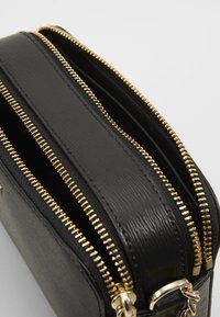 Bustina in pelle nera con zip double gold, superficie texturizzata e hardware lucido. Design compatto per praticità e stile.