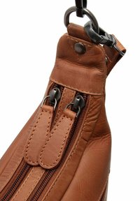 Bruine leren tas met twee ritscompartimenten, voorzien van donkere ritshardware en een robuust bevestigingspunt voor de schouderriem. Strakke textuur en doordacht ontwerp.