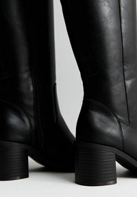 Stivali neri in pelle fino al ginocchio con finitura liscia, zip laterale e tacco impilato e testurizzato. Design classico con punta tonda.