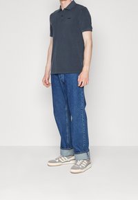 Czarny polo z guzikami, w połączeniu z jasnoniebieskimi dżinsami. Szare sneakersy z białymi paskami i gumową podeszwą.