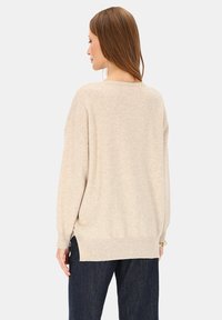 Beżowy sweter z dzianiny o luźnym kroju, opuszczanych ramionach i bocznych rozcięciach. Miękka tekstura, długie rękawy i okrągły dekolt.