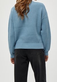 Maglione blu chiaro lavorato a maglia con un design a coste testurizzato e spalle ribassate; abbinato a jeans in denim neri e una cintura aderente.