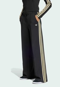 Svarta vida byxor med gula tre-stripsdetaljer ned längs sidorna, med fickor och elastisk midja. Logotyp på benet.