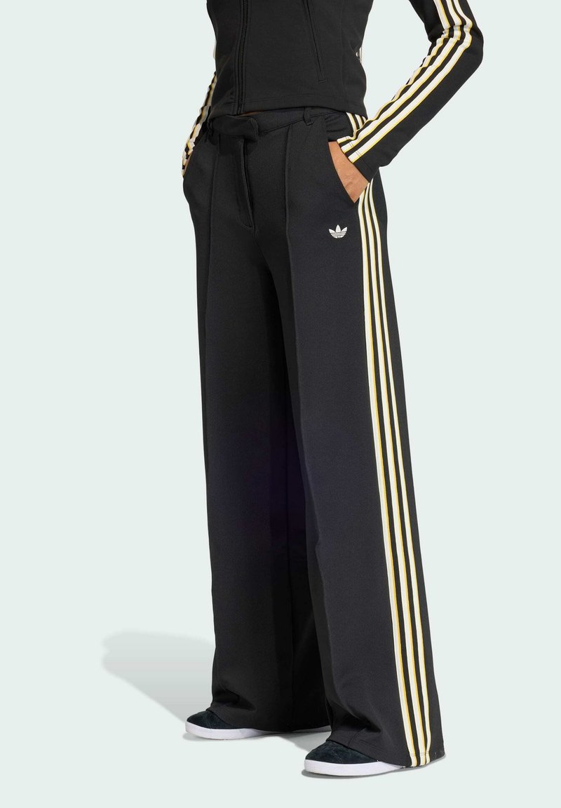 Svarta vida byxor med gula tre-stripsdetaljer ned längs sidorna, med fickor och elastisk midja. Logotyp på benet.