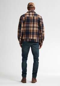 Brun og marineblå rutenbånds flannel skjorte, afslappet pasform, knapmanchetter, parret med mørke denim jeans og brune støvler. Enkel, funktionel design.