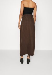 Falda maxi de mezclilla marrón con un diseño recto, que presenta dos bolsillos traseros y un dobladillo que se estrecha ligeramente hacia la parte inferior.