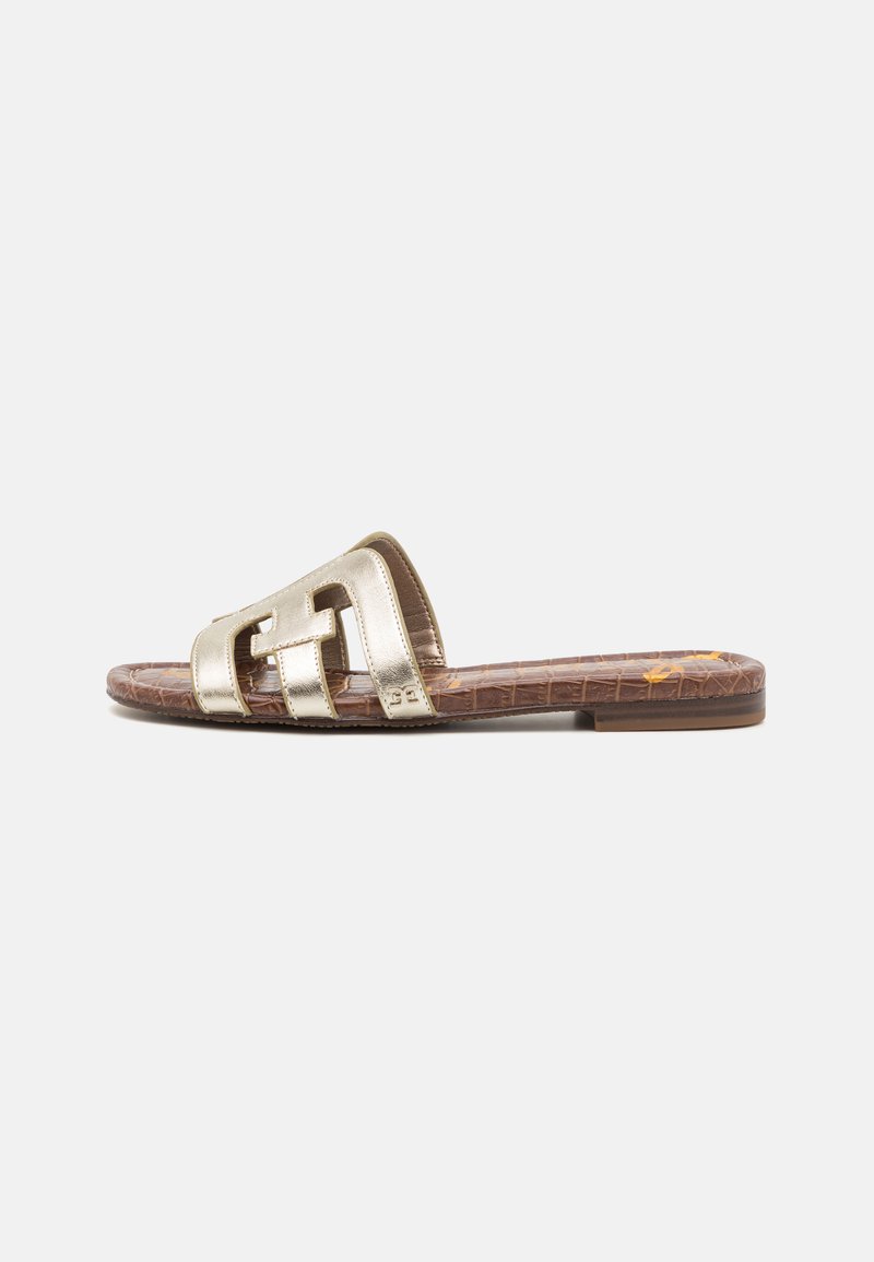 Sandal com numeração metálica dourada e design de dupla alça. Sola texturizada castanha com padrão de crocodilo. Salto baixo e plano.