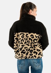 Giacca in pile nera e beige con parte superiore nera e parte inferiore a stampa leopardata. Presenta un colletto alto e una vestibilità rilassata.