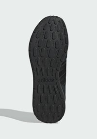 Czarna podeszwa sportowego buta z teksturowaną gumową powierzchnią z okrągłymi i liniowymi wzorami, oznaczona napisem „adidas” w pobliżu pięty.