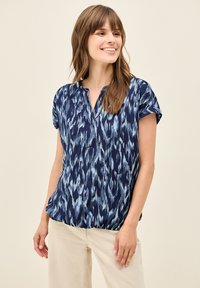 Blusa blu navy realizzata in un tessuto leggero e strutturato, con un motivo simile all'acqua in diverse tonalità di blu. Maniche corte e vestibilità morbida.
