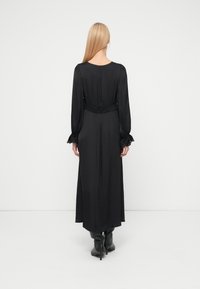 Black maxi dress with long sleeves, textured fabric, cinched waist, and buttoned cuffs, featuring a sleek, flowing silhouette.