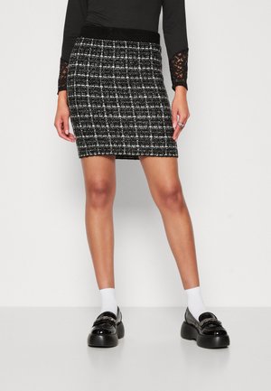 Zwart-wit tweed minirok met een aansluitende tailleband en gestructureerde vorm, gecombineerd met zwarte loafers en witte sokken.