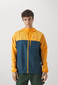 Chaqueta con bloques de color en amarillo y azul verdoso, con cierre de cremallera en la parte delantera, capucha ajustable, puños elásticos y un bolsillo en el pecho. Presenta un patrón decorativo.