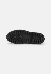 Semelle extérieure en caoutchouc noir avec des sculptures profondes et des motifs étoilés, forme courbée, surface texturée et petit logo près du talon.