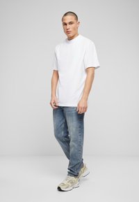 Tricou alb cu mânecă scurtă și decolteu rotund, combinat cu blugi drepți de culoare deschisă și adidași bej.