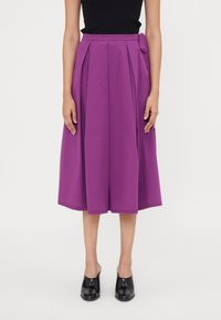Falda plisada morada con detalle de cintura atada, hecha de una tela suave. Longitud a media pantorrilla y silueta acampanada, combinada con mules negros.