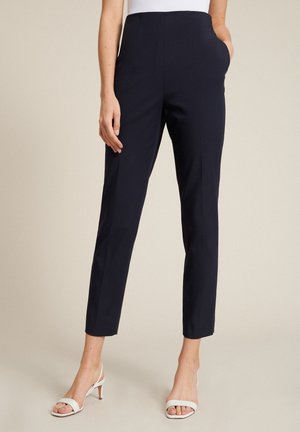 Pantalons tailleurs bleu marine, taille haute, avec poches latérales et coupe ajustée. Tissu lisse au design épuré, associés à des talons blancs à lanières.